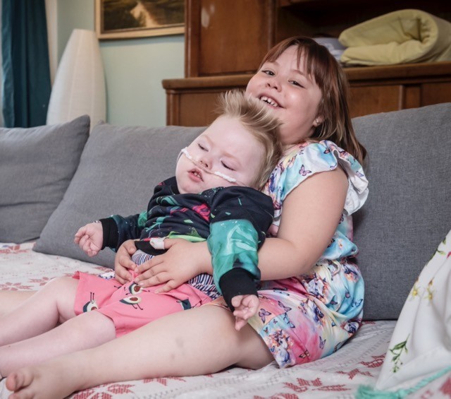 Lea blickt lächelnd in die Kamera mit ihrem Bruder Theo auf dem Schoss