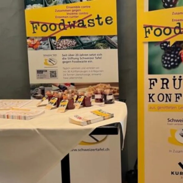 Zwei gelbe Informationsbanner zur Schweizer Tafel mit Texten zu Foodwaste und Früchtekonfitüre, davor ein Tisch mit Flyern und kleinen Gläsern gefüllt mit Konfitüre..