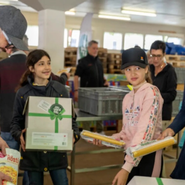 Mehrere Personen, darunter Kinder und Erwachsene, packen gemeinsam Lebensmittelboxen.