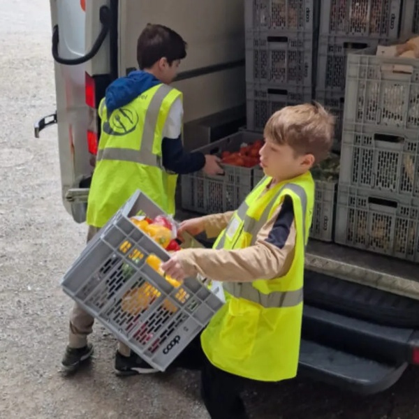 Zwei Kinder mit gelben Schweizer Tafel Warnwesten laden Kisten mit Nahrungsmittel aus einem weissen Lieferwagen aus.